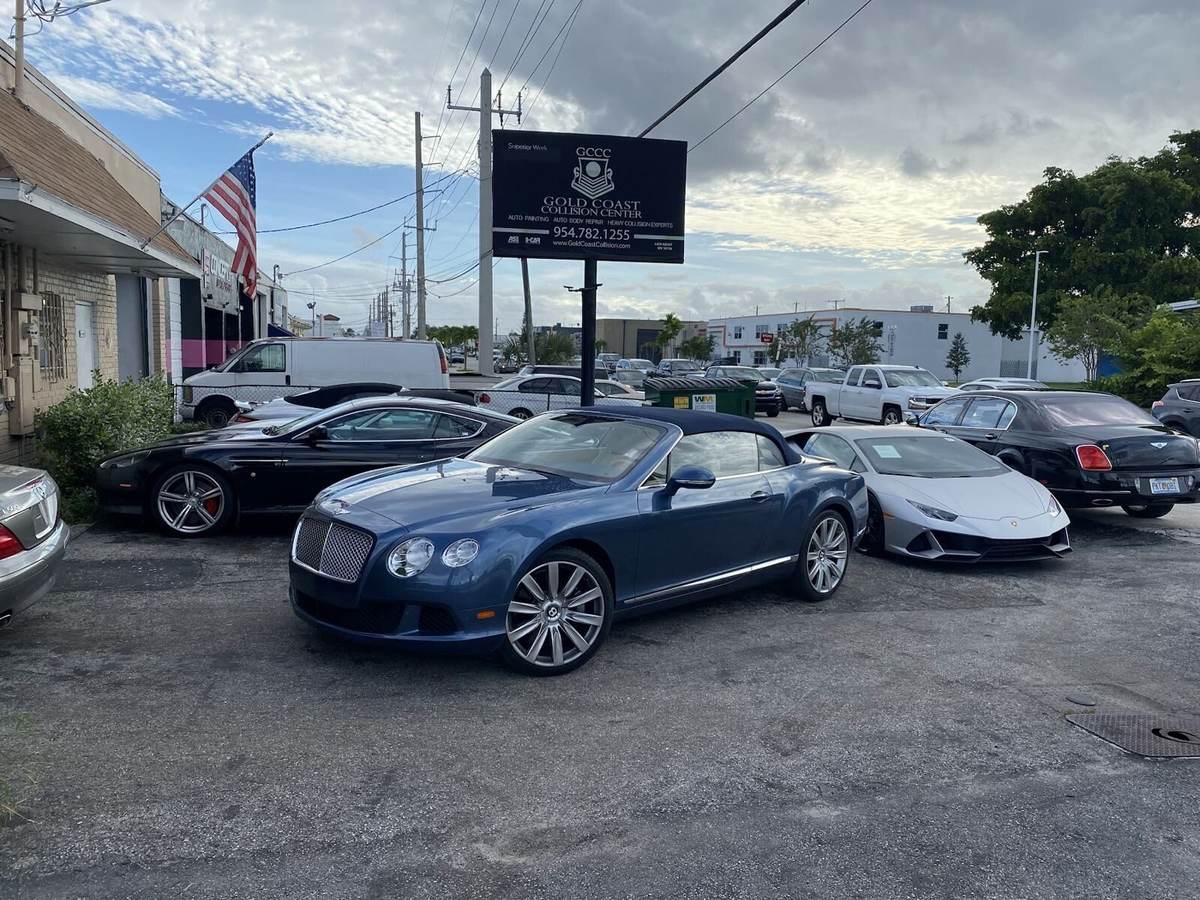 Gold Coast Collision Center sign on S Dixie Hwy in Pompano Beach with a Bentley convertible and a Lamborghini Huracán in the lot