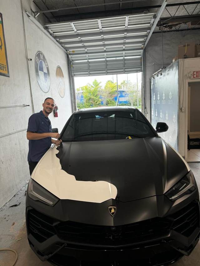 Technician working on a matte-black Lamborghini Urus at Gold Coast Collision Center