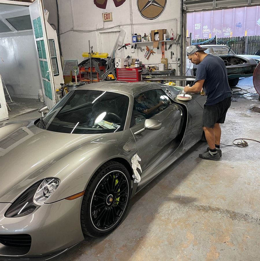 Technician machine-polishing the door of a silver Porsche 918 Spyder inside Gold Coast Collision Center in Pompano Beach