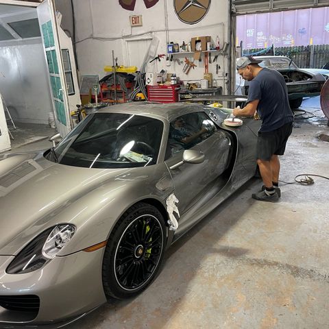 Technician machine-polishing the door of a silver Porsche 918 Spyder inside Gold Coast Collision Center in Pompano Beach